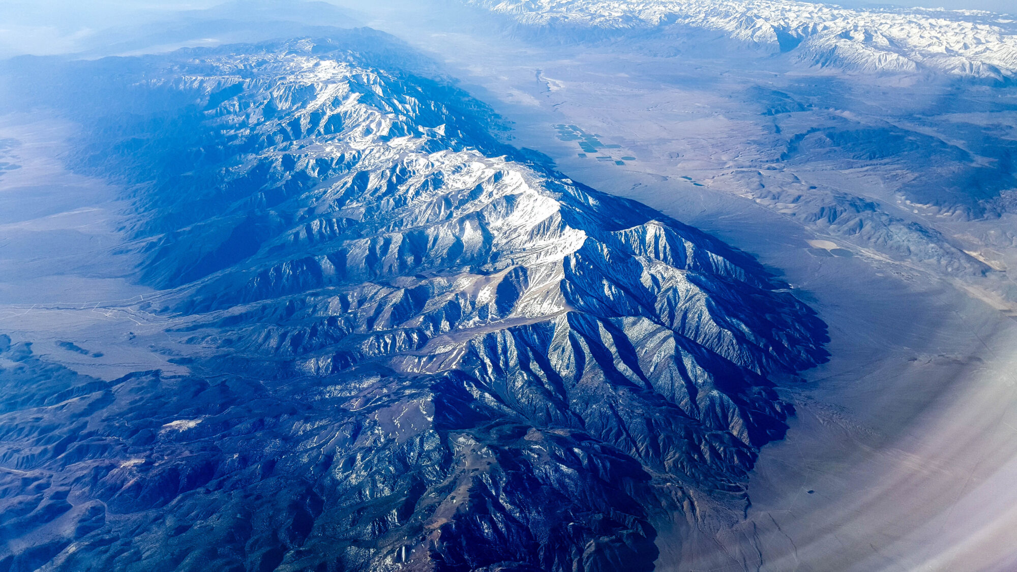 Large, impressive snow capped mountain ridge rising from valley on each side near Montgomery Pass, Nevada (looking south from airplane window)