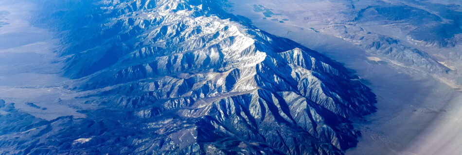 Large, impressive snow capped mountain ridge rising from valley on each side near Montgomery Pass, Nevada (looking south from airplane window)